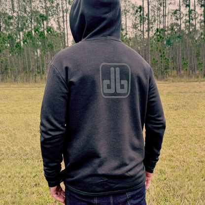 Person wearing a dark hoodie with a db ogo on the back, standing in an open field with trees in the background.